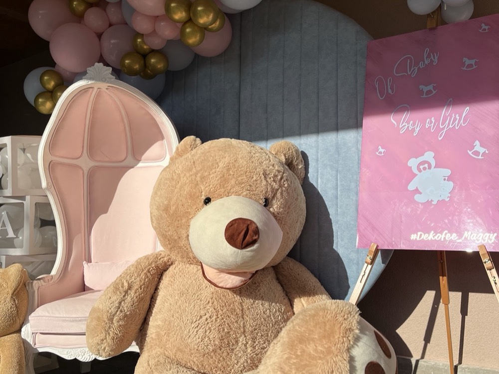 Grosser Teddybär vor einem rosa Sessel und Ballons